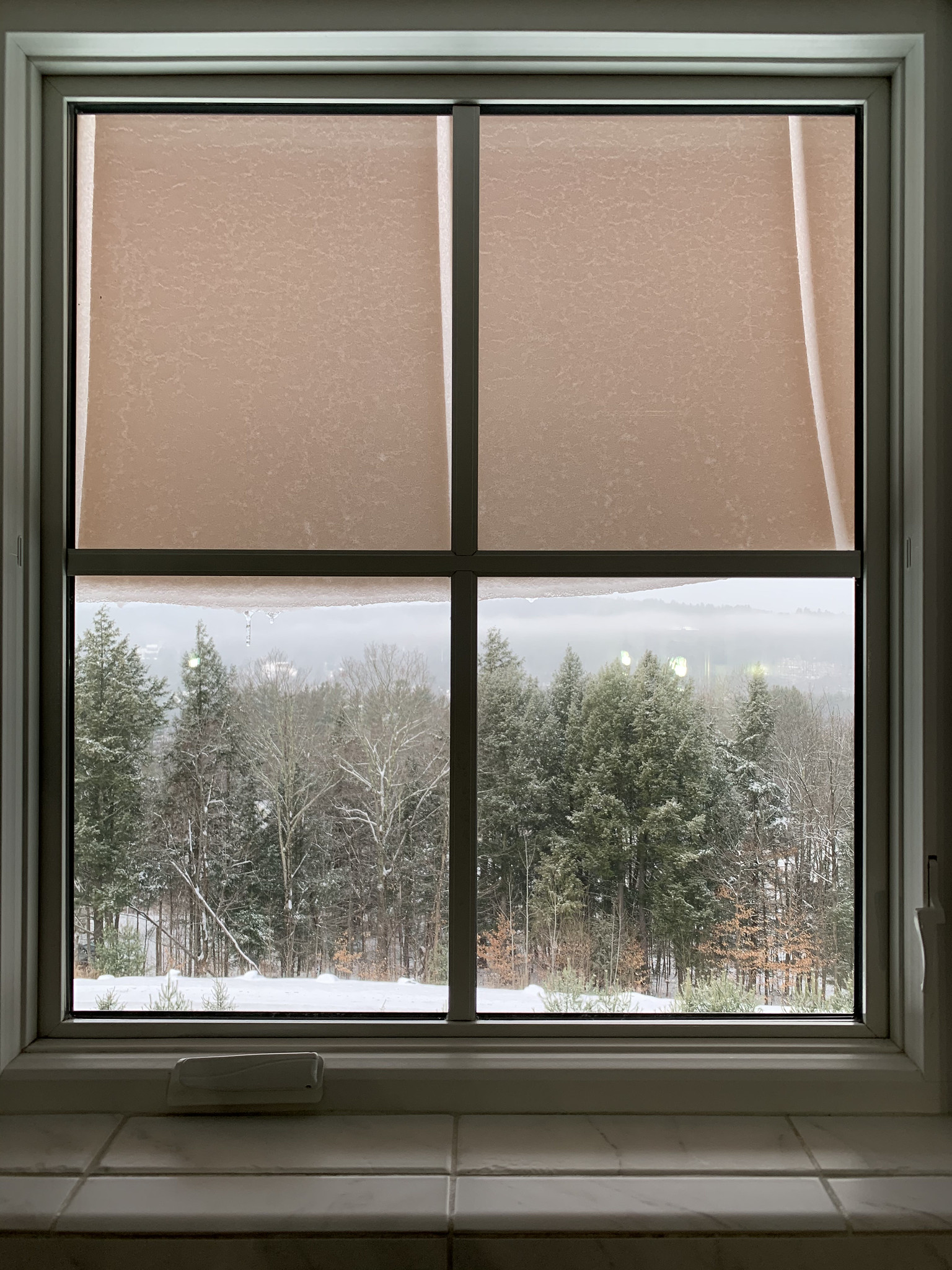 A slab of snow hanging from the roof visible through a window.